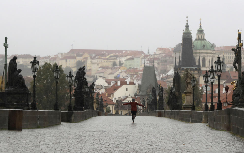 A man runs across an empty medieval Charles Bridge in Prague, Czech Republic, Wednesday, Oct. 14, 2020. The Czech Republic has imposed a new series of restrictive measures in response to a record surge in coronavirus infections. Starting Wednesdays all bars and restaurants can only sell takeaway while drinking of alcohol is banned at public places. (AP Photo/Petr David Josek)