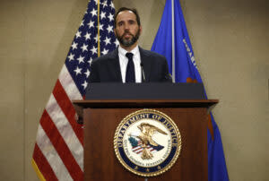 A man in a suit at a podium with an emblem saying Department of Justice.