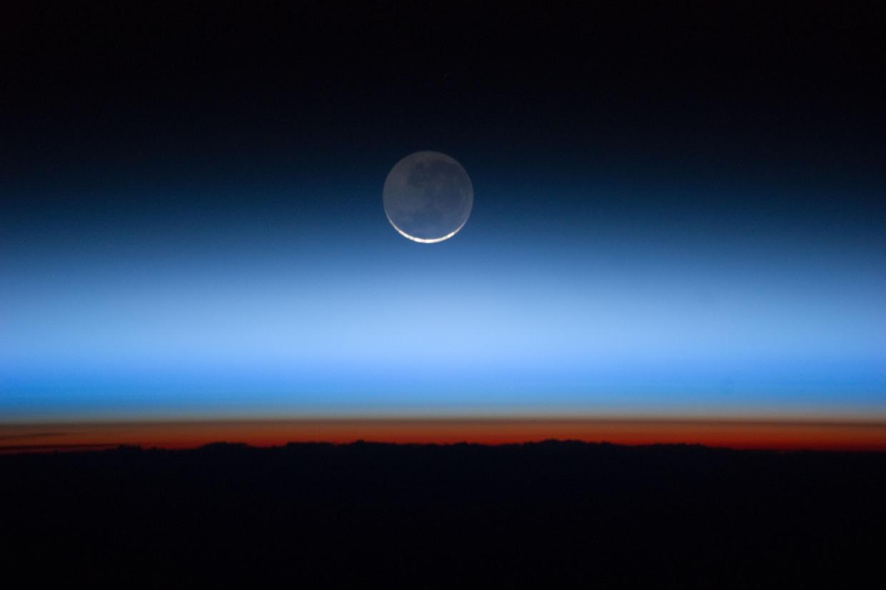 This undated image made available by NASA and photographed by the Expedition 28 crew aboard the International Space Station shows the moon at center with the limb of Earth near the bottom transitioning into the orange-colored troposphere, the lowest and most dense portion of the Earth's atmosphere.