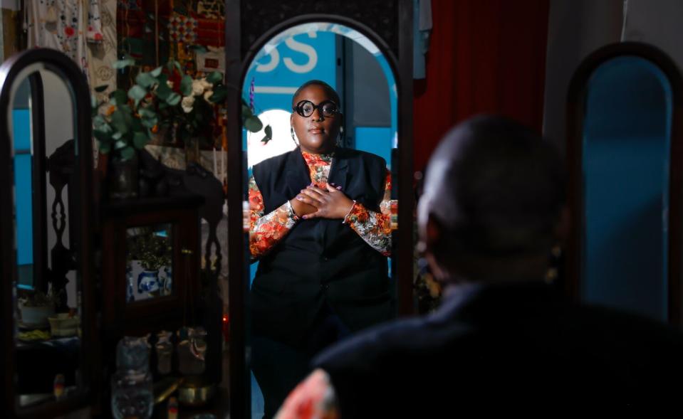 A Black person reflected in a mirror with their hands on their chest.