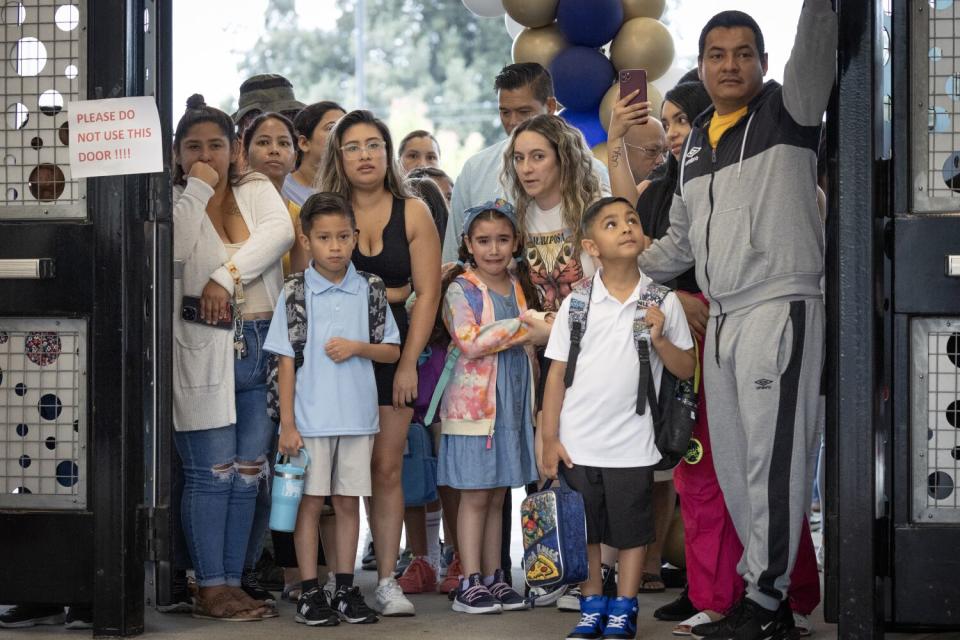 A group of children and parents stand at a school entrance.