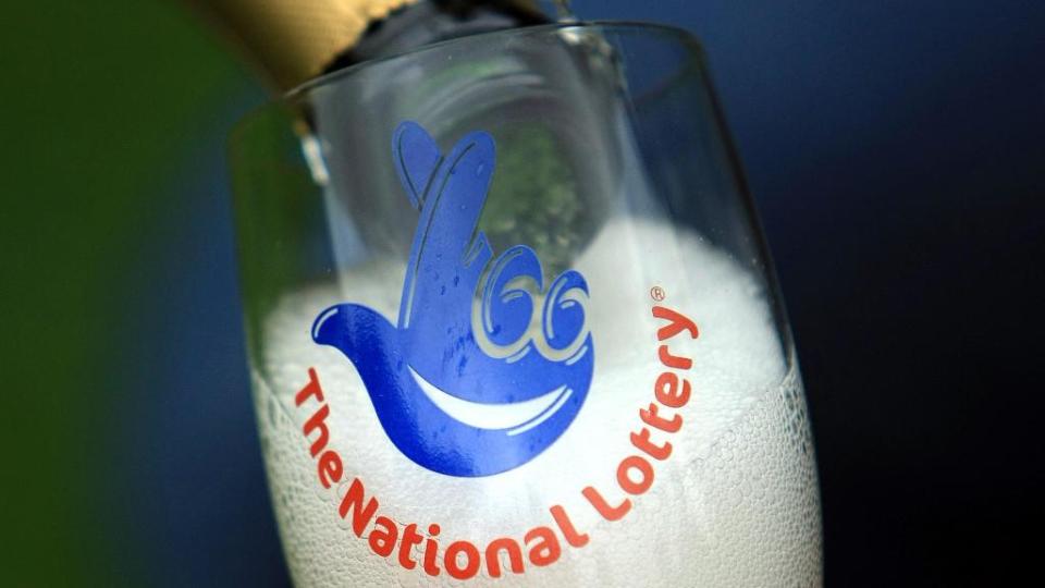 Champagne is poured into a National Lottery branded champagne glass flute.