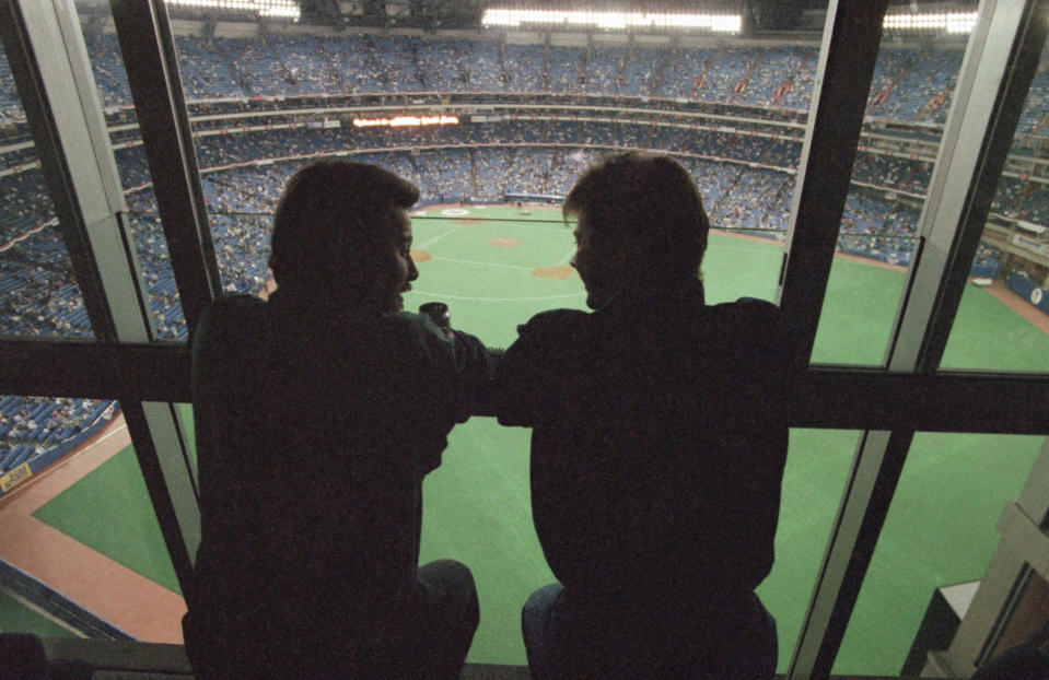 FILE - In this Oct. 22, 1992, file photo, spectators look out at the field from a window of the SkyDome Hotel before Game 5 of the World Series between the Toronto Blue Jays and the Atlanta Braves in Toronto. All 30 Major League Baseball teams will train at their regular-season ballparks for the pandemic-shortened season after the Blue Jays received a Canadian federal government exemption on Thursday, July 2, 2020, to work out at Rogers Centre. Toronto will move camp from its spring training complex in Dunedin, Fla., where players reported for intake testing. The Blue Jays will create a quarantine environment at Rogers Centre and the adjoining Toronto Marriott City Centre Hotel, formerly the SkyDome, which overlooks the field. (AP Photo/Rusty Kennedy, File)