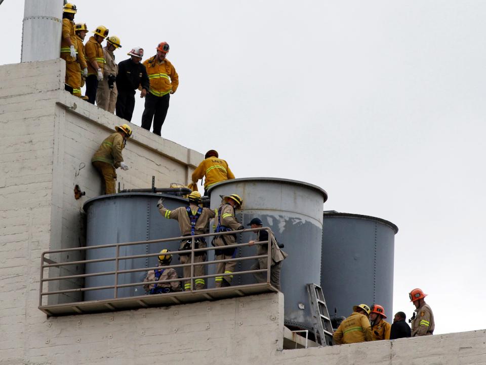 Photo of large water tanks and many firefighters standing around and on them on the roof.