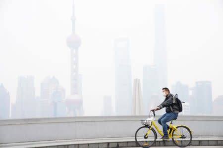 A man wearing a face mask rides a bicycle on a bridge in front of the financial district of Pudong covered in smog during a polluted day in Shanghai, China November 22, 2017. REUTERS/Aly Song