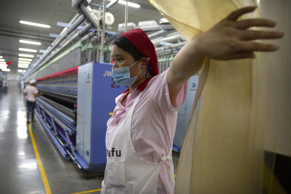 A worker holds open a plastic curtain at a Huafu Fashion plant, as seen during a government organized trip for foreign journalists, in Aksu in western China's Xinjiang Uyghur Autonomous Region, Tuesday, April 20, 2021. A backlash against reports of forced labor and other abuses of the largely Muslim Uyghur ethnic group in Xinjiang is taking a toll on China's cotton industry, but it's unclear if the pressure will compel the government or companies to change their ways. (AP Photo/Mark Schiefelbein)