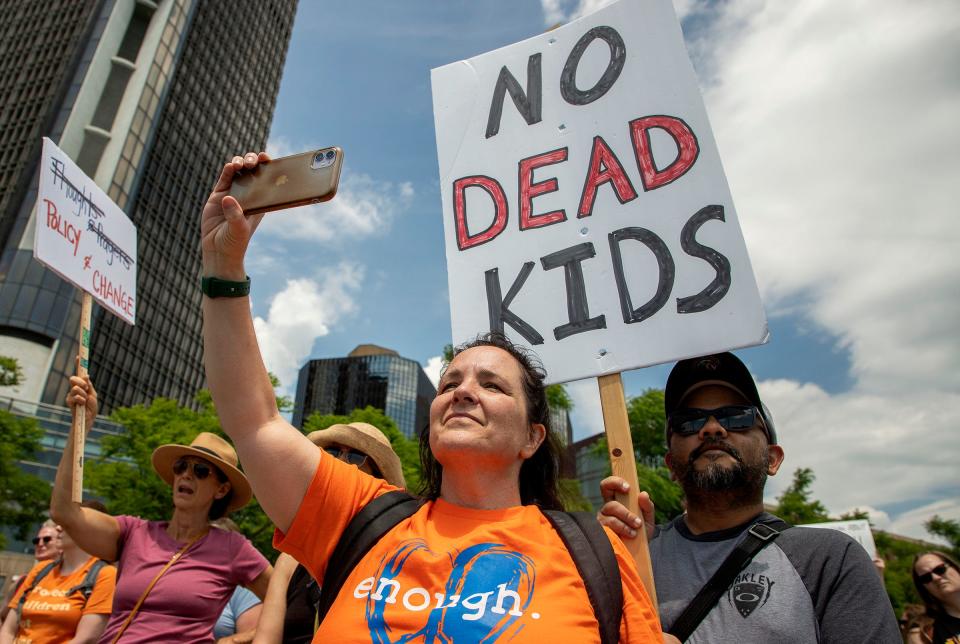 Vika Vantram, of Heartland, left, holds a sign as his wife, Joanna, a teacher for the Howell Public Schools system records speakers as people fill Detroit's riverfront on Saturday, June 11, 2022, as they listen to speakers and march in the March for Our Lives Detroit event. Speakers came to the microphone one by one and demanded that lawmakers enact gun control laws to keep these tragedies from happening again.