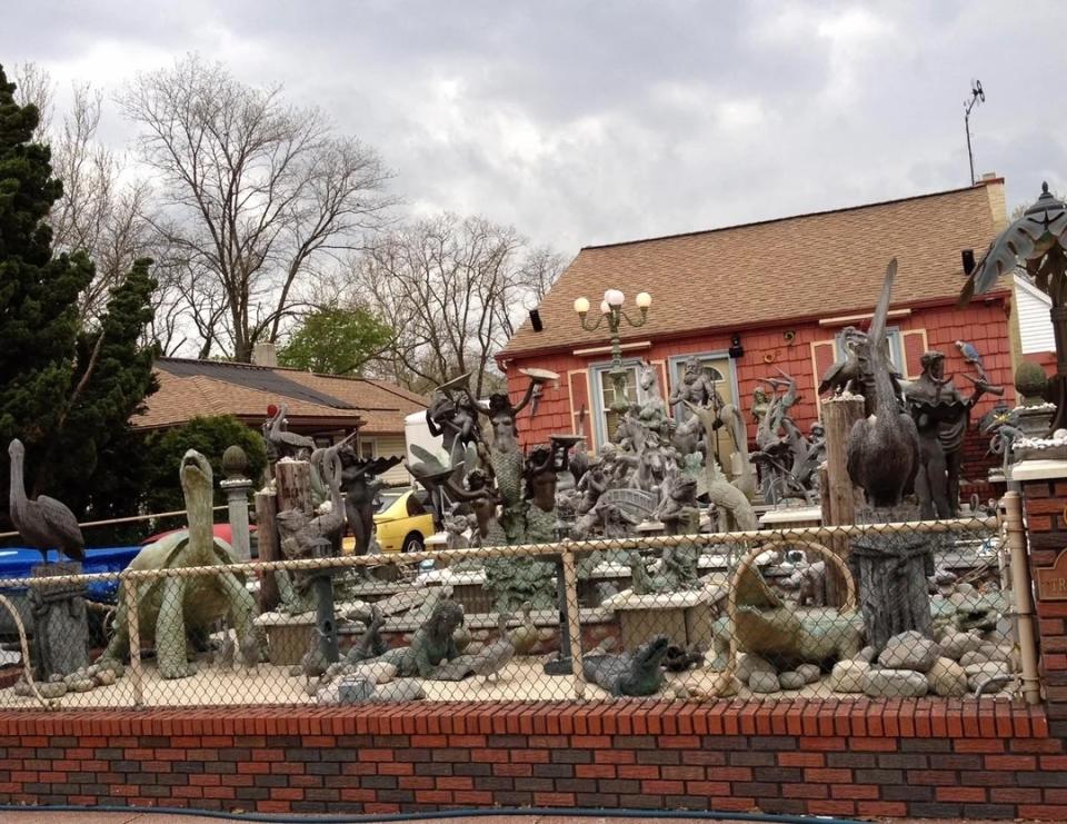 A yard filled with numerous statues of animals, mythical creatures, and various objects, all enclosed within a fence in front of a house