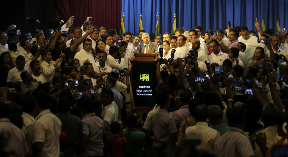 Sri Lanka's reinstated prime minister Ranil Wickeremesinghe, center, surrounded by his loyal lawmakers and supporters speaks after assuming duties in Colombo, Sri Lanka, Sunday, Dec. 16, 2018. Sri Lanka's president has reappointed Ranil Wickremesinghe as prime minister, nearly two months after firing him and setting off weeks of political stalemate. (AP Photo/Eranga Jayawardena)