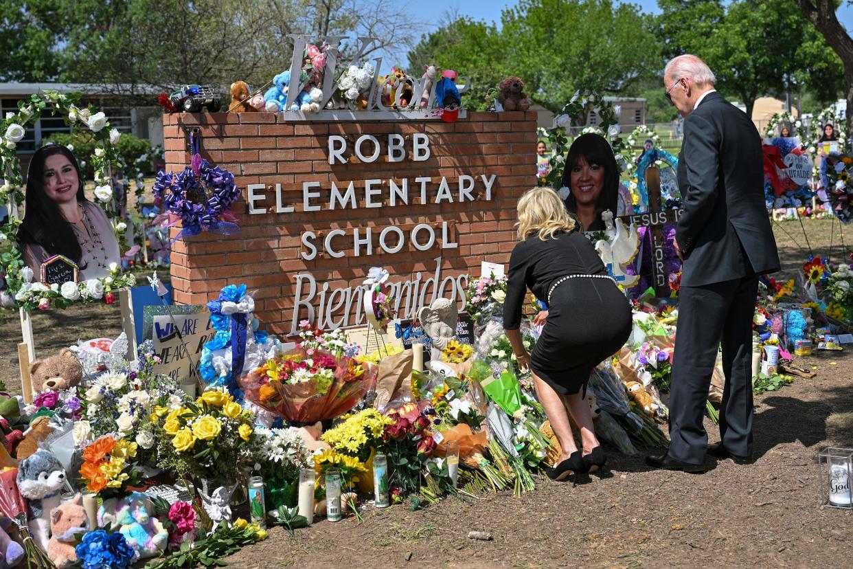 Jill Biden, wearing a black dress, lays flowers at a memorial situation around a brick signs that reads: Robb Elementary School.