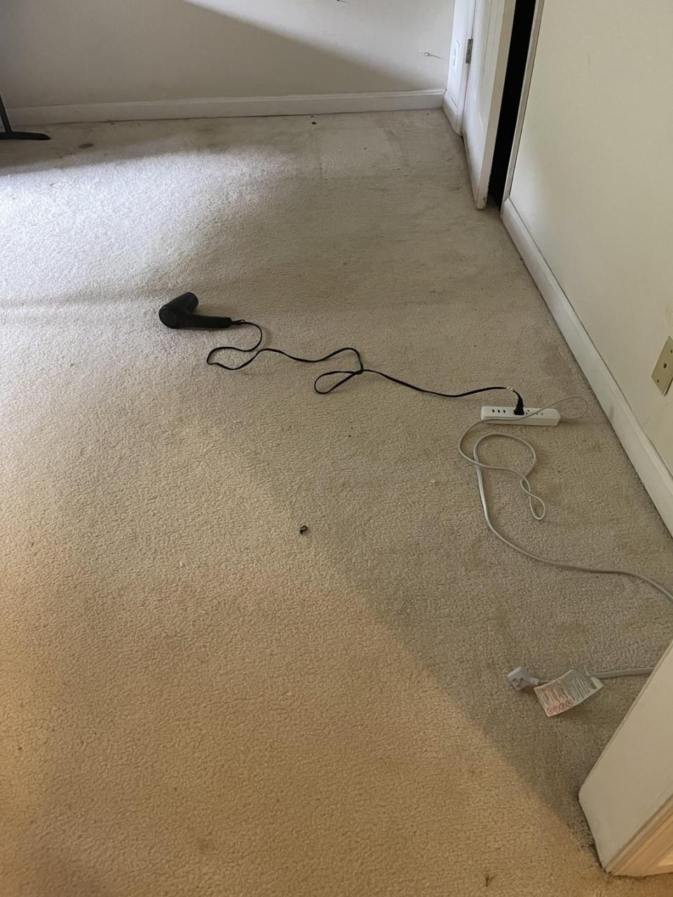 A vacuum cleaner with an attached cord is lying on a carpeted floor partially plugged into a power strip