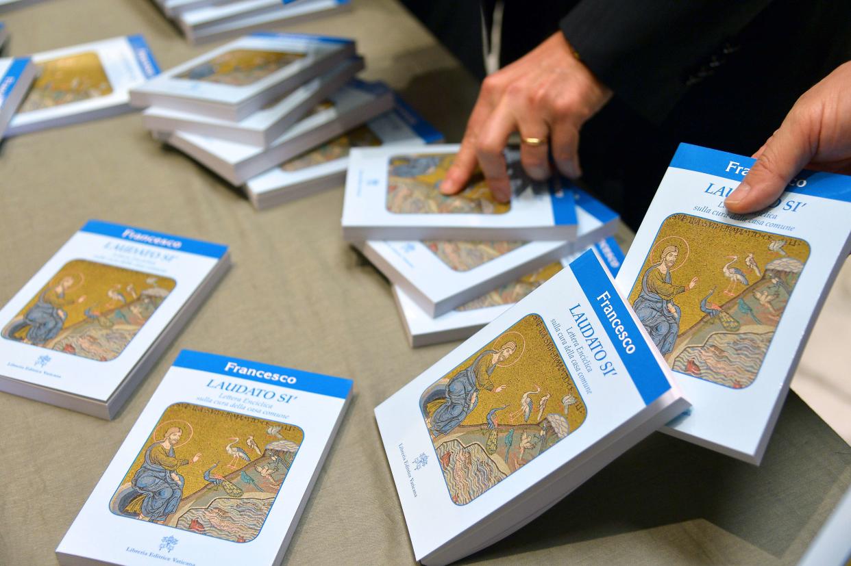 People hold copies of Pope Francis' encyclical, a collection of principles to guide Catholic teaching, entitled "Laudato Si" during its official presentation, on June 18, 2015 at the Sinod hall at the Vatican.