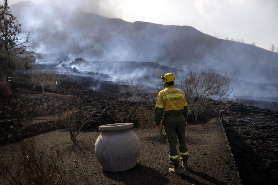 A municipal worker looks as smoke rises after a volcano erupted, near El Paso on the island of La Palma in the Canaries, Spain, Tuesday, Sept. 21, 2021. A dormant volcano on a small Spanish island in the Atlantic Ocean erupted on Sunday, forcing the evacuation of thousands of people. Huge plumes of black-and-white smoke shot out from a volcanic ridge where scientists had been monitoring the accumulation of molten lava below the surface. (AP Photo/Emilio Morenatti)