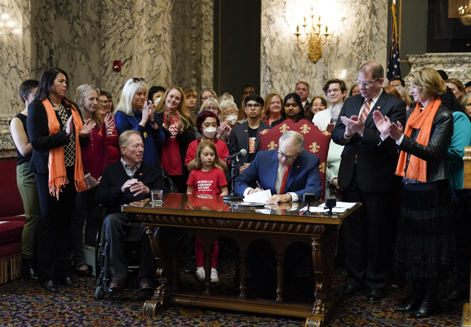 Washington Gov. Jay Inslee signs House Bill 1240, which prohibits the manufacture, importation, distribution and sale of semi-automatic assault-style weapons in the state, Tuesday, April 25, 2023, at the Capitol in Olympia, Wash., as Rep. Strom Peterson, D-Edmonds, the bill's primary sponsor, and Sen. Patty Kuderer, D-Bellevue, look on at right. (AP Photo/Lindsey Wasson)