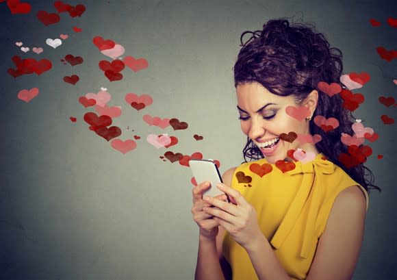 Artist's rendering of romantic hearts flying out of phone as woman smiles