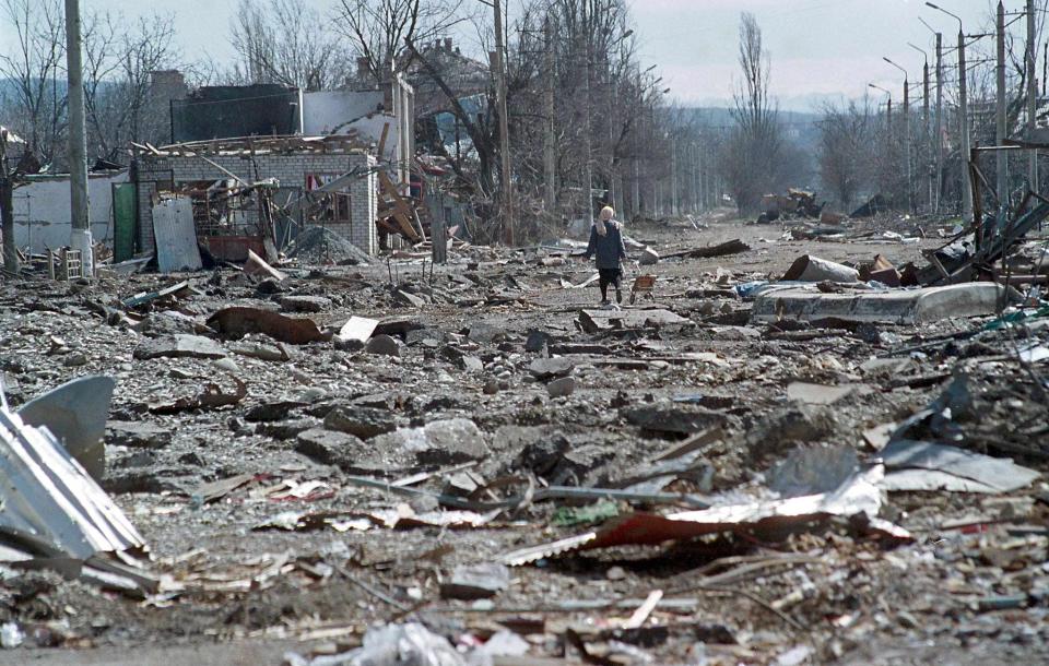 A Chechen woman pulls a cart behind her as she walks through the rubble of a near-flattened street.