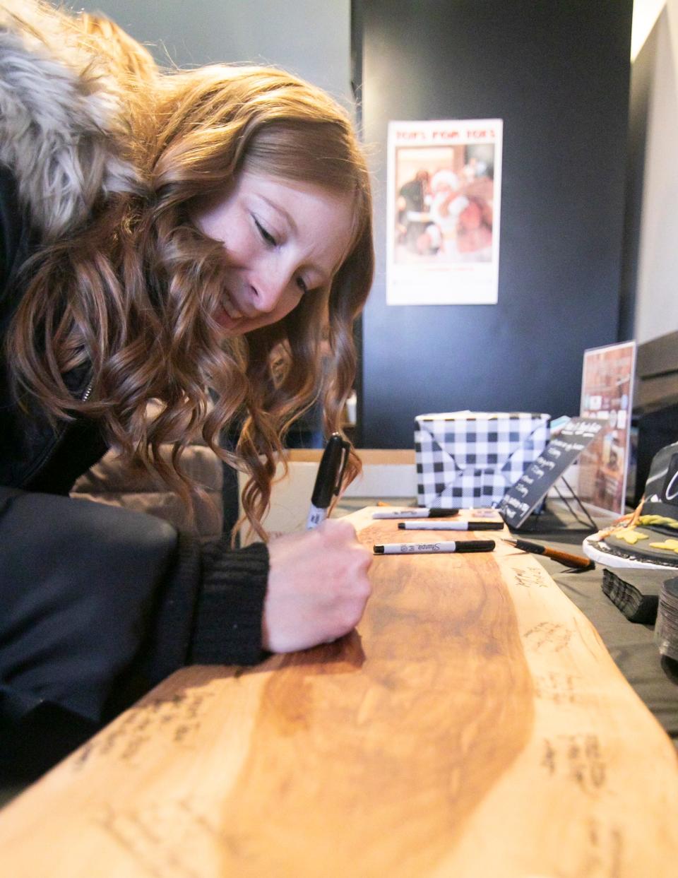 Jennifer Rote of Brighton signs well wishes on a large cutting board that will be hung on the wall of the newly opened Captain's on Main in downtown Brighton Friday, Nov. 18, 2022.