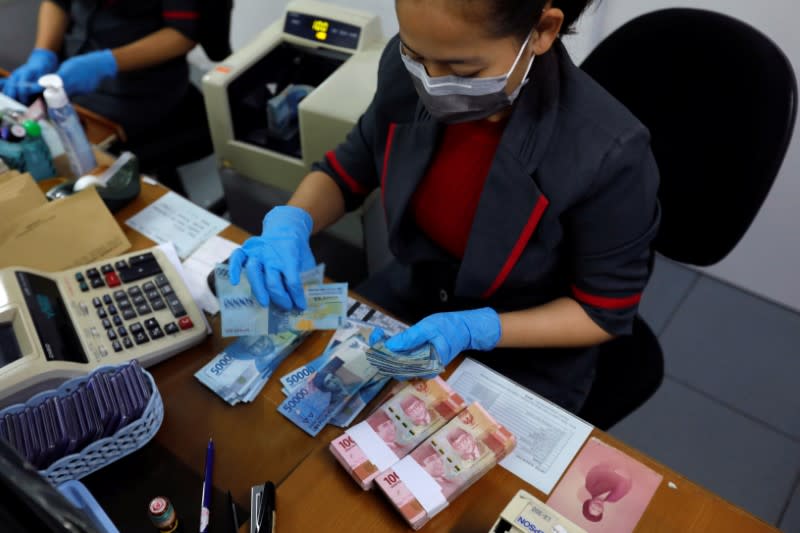 An employee wearing a face mask and synthetic gloves counts Indonesia's rupiah banknotes at a currency exchange office amid the spread of coronavirus disease (COVID-19) in Jakarta