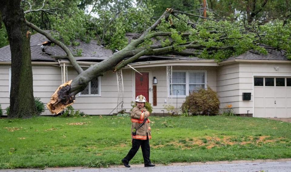 A tree limb lies on top of a house as an Overland Park firefighter crosses the road after checking the residence for occupants on Friday, July 14, 2023, in Overland Park, Kan.