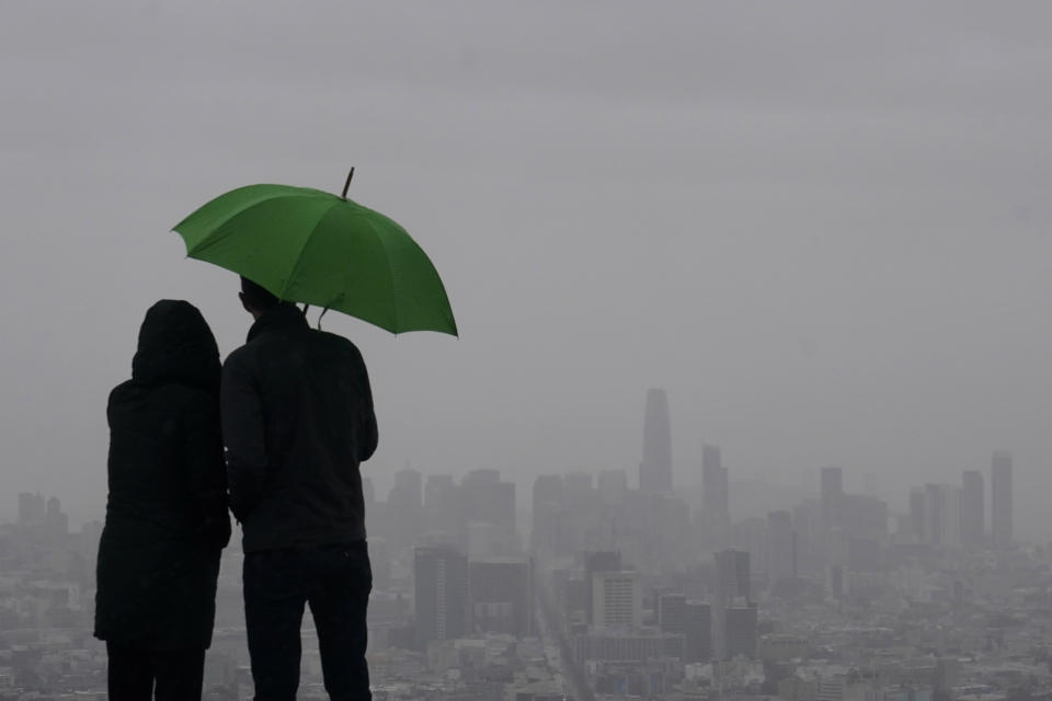 People stand under an umbrella while looking toward the skyline from Twin Peaks in San Francisco, Thursday, March 9, 2023. California is bracing for the arrival of an atmospheric river that forecasters warn will bring heavy rain, strong winds, thunderstorms and the threat of flooding even as the state is still digging out from earlier storms. (AP Photo/Jeff Chiu)