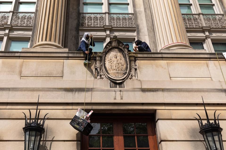 Pro-Palestinian student protesters pull up a crate with pizza boxes to a balcony at Columbia University. AFP via Getty Images
