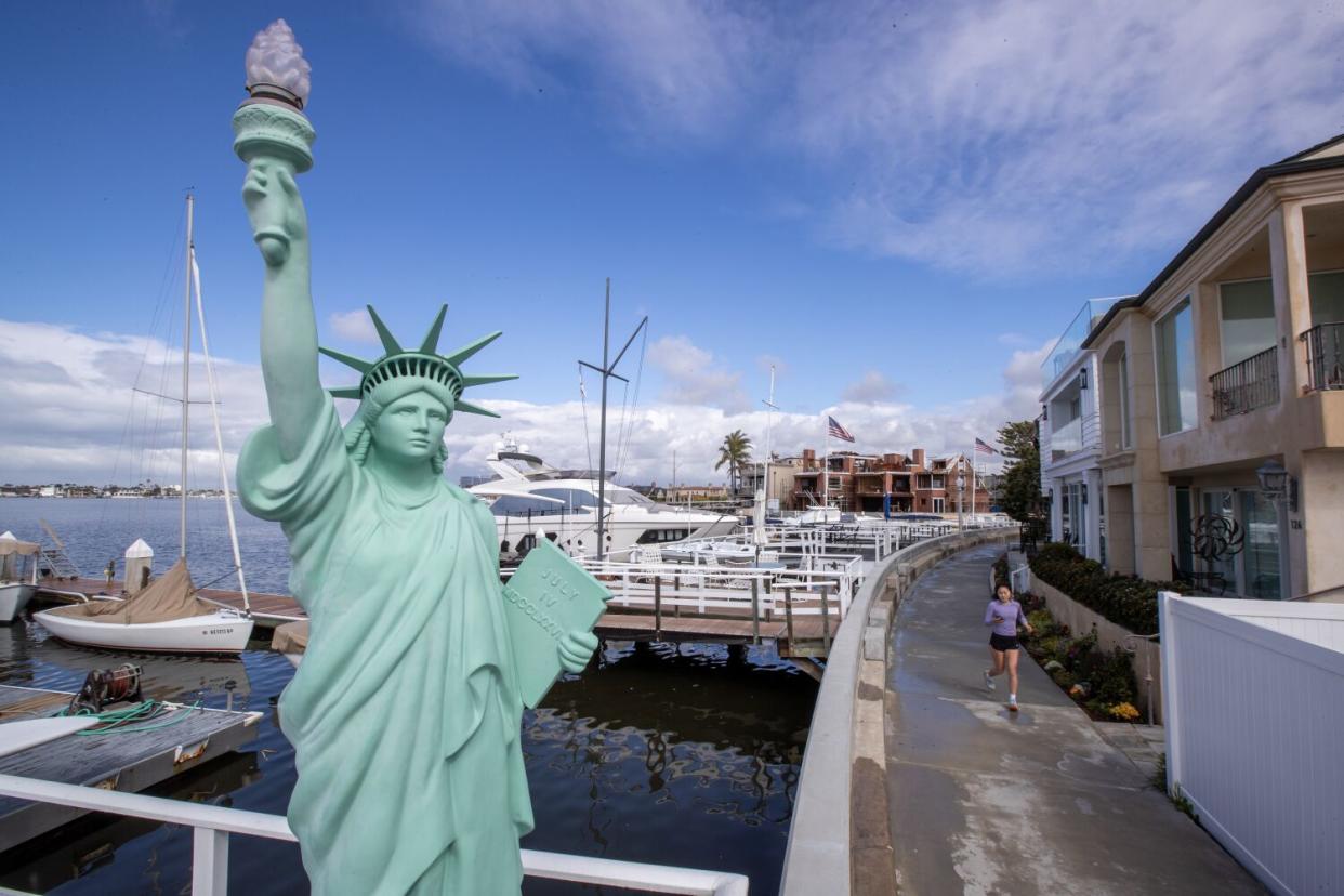 A jogger passes a decorative Statue of Liberty on the Balboa Island boardwalk.