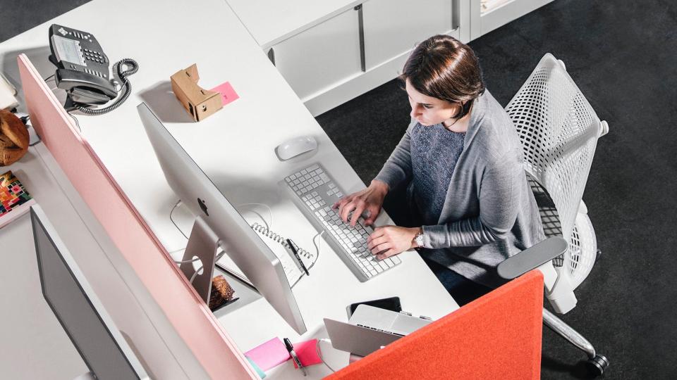 A woman sits at a desk in a Herman Miller chair.