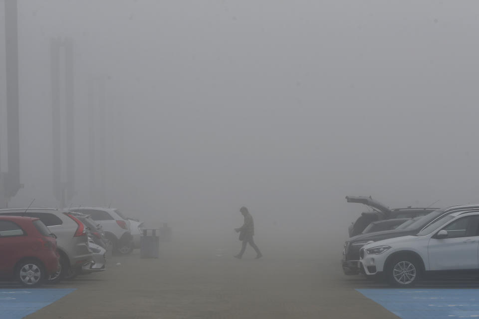 A man crosses the car park in thick fog outside the COP25 summit in Madrid, Spain, Tuesday, Dec. 10, 2019. The 2-week global U.N. sponsored climate change conference is taking place in Madrid. (AP Photo/Paul White)