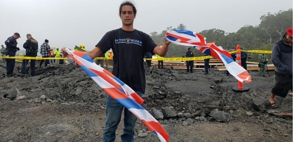 This photo provided by Andre Perez shows Oli Turalde holding a torn Hawaii state flag on Friday Sept. 6, 2019 on Mauna Kea, on the big island of Hawaii, where opponents of a giant telescope have been camped to block construction on a mountain some Native Hawaiians consider sacred. Crews arrived to demolish a small wooden house built near the protest camp. Officials say they had no choice but to cut a Hawaii flag that was on a barricade over the structure's door. (Andre Perez via AP)