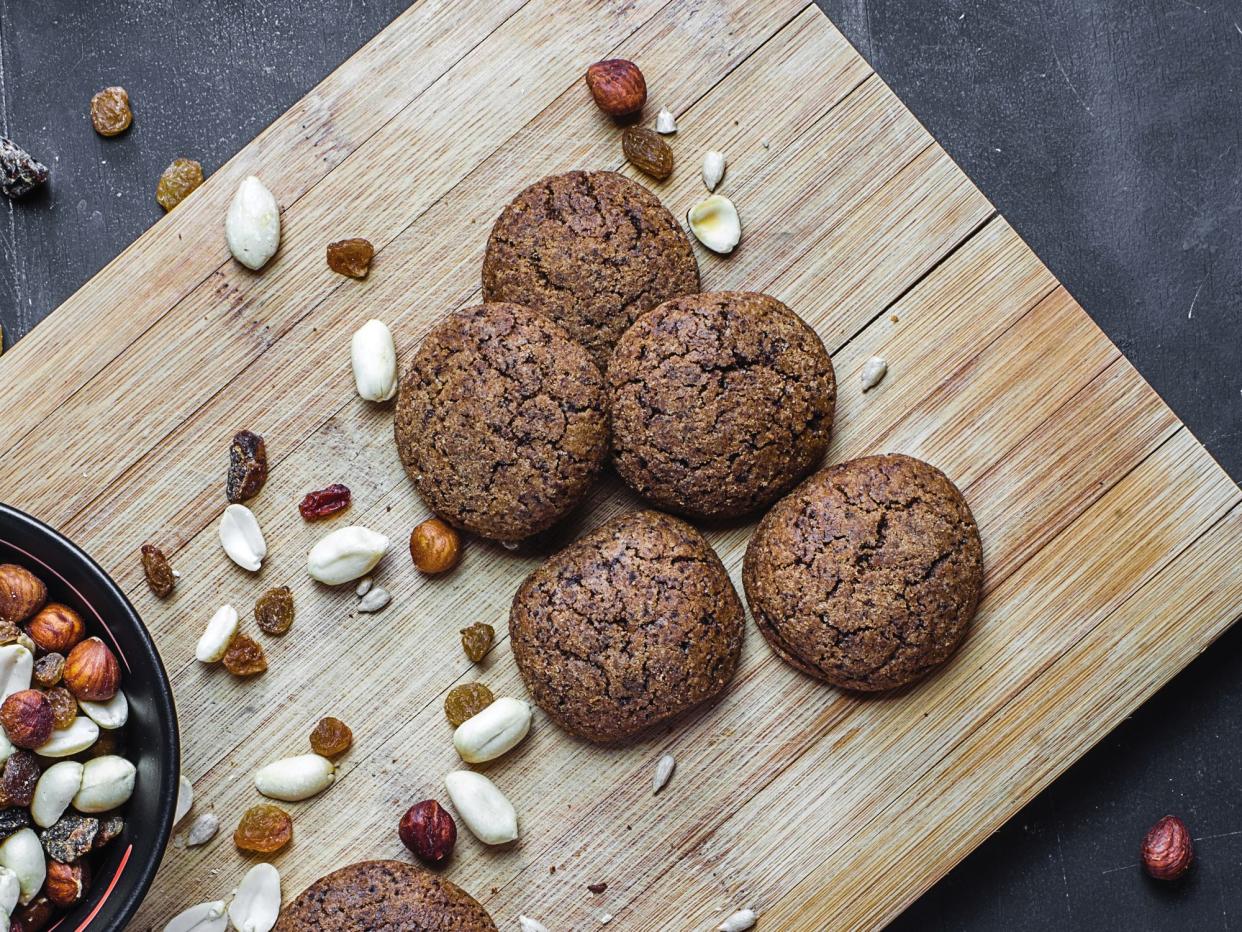 Several types of nuts near the baked pastry. Black bowl with nuts and dried fruits near the appetizing biscuits. Top view of oatmeal biscuits.