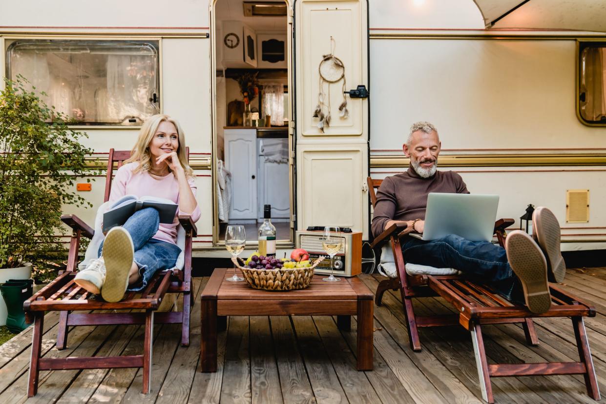 Portrait of senior married caucasian couple having rest on the deck chairs with food and wine just against their caravan home