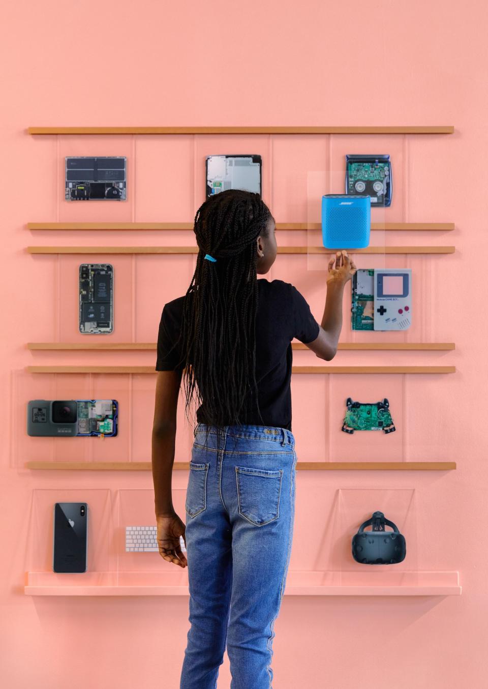 A young girl studies the inner makings of various devices on the wall.