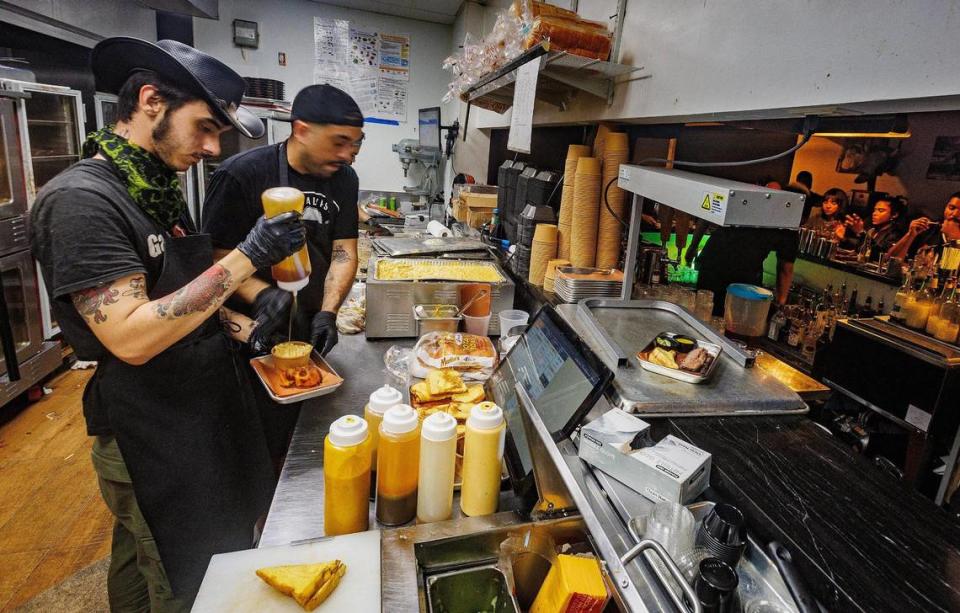 Los cocineros de línea Bryan Rodríguez García (a la izquierda) y José Acevedo apresurándose a preparar algunos pedidos en la cocina de Apocalypse BBQ en Kendall.