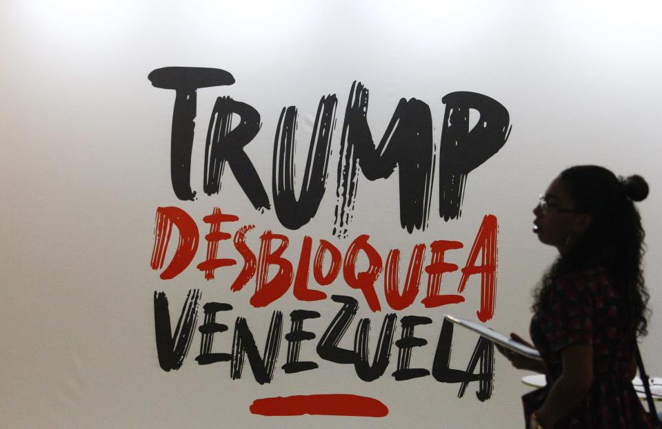A woman walks next to a sign that reads in Spanish "Trump, Unblock Venezuela," a reference to the Venezuelan government view that U.S. sanctions, aimed at toppling President Nicolas Maduro, are driving the country's economic problems, at the Sao Paulo Forum in Caracas, Venezuela, Friday, July 26, 2019. (AP Photo/Leonardo Fernandez)