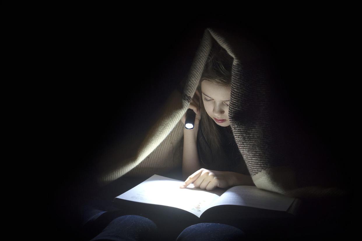 Girl with a flashlight reading a book.