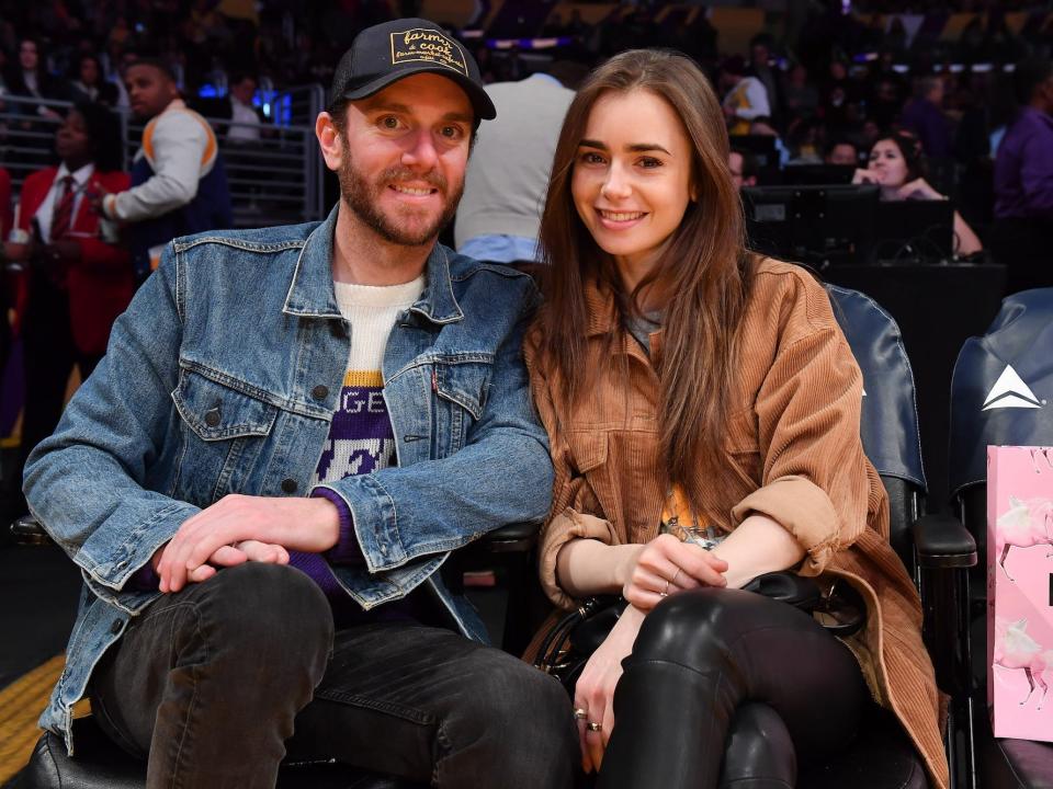Charlie McDowell and Lily Collins smile at a basketball game.