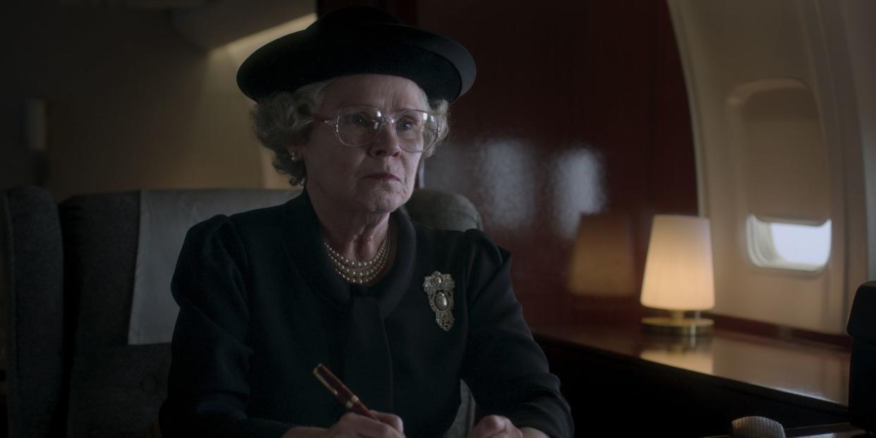 queen elizabeth wearing a hat and glasses sitting at a desk