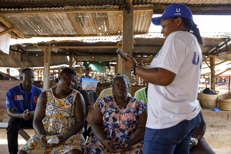 Rita Quansah, right, from Uniti Networks, coaches farmers on how to navigate its platform of applications, from pensions that encourage saving to agriculture apps, at a market in Hohoe, Ghana, Wednesday, April 18, 2024. (AP Photo/ Misper Apawu)