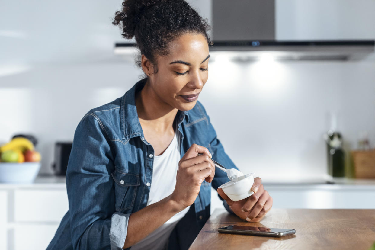 Woman eating yogurt sitting in kitchen at home