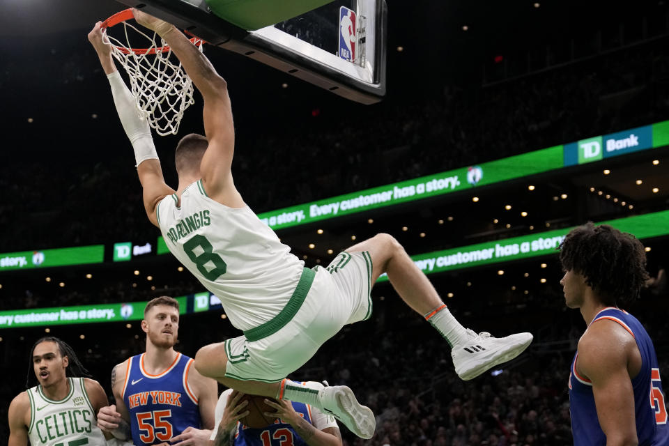 Boston Celtics center Kristaps Porzingis (8) hangs on the rim after a dunk against the New York Knicks during the second half of a preseason NBA basketball game, Tuesday, Oct. 17, 2023, in Boston. (AP Photo/Charles Krupa)