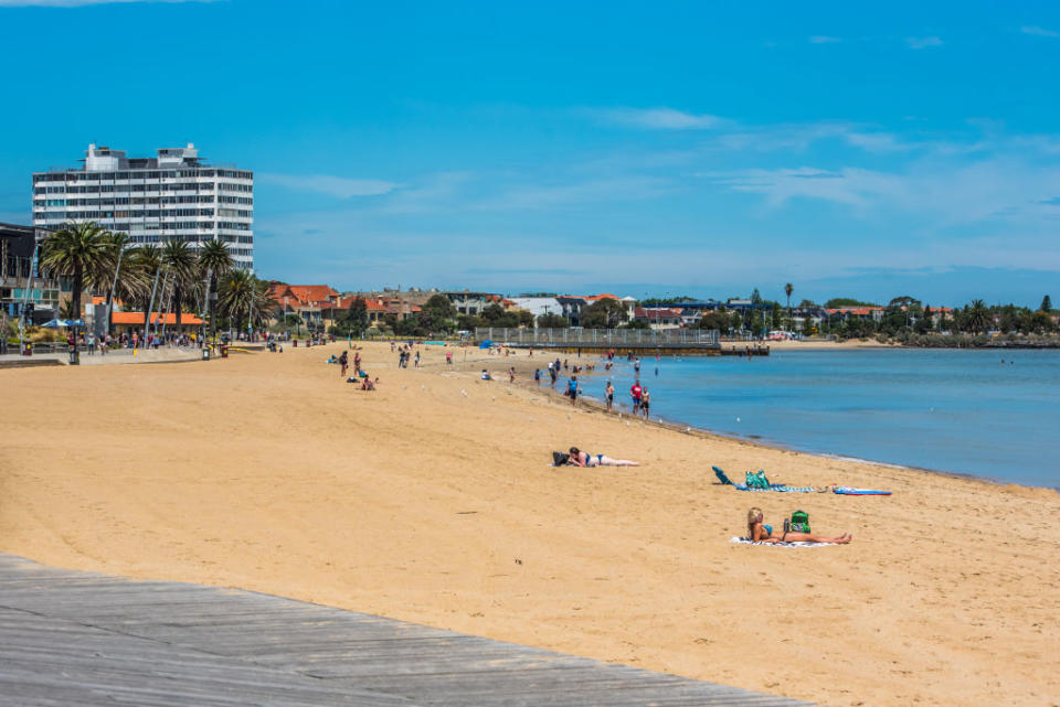 People sit on the sand at St Kilda beach on a sunny day. 