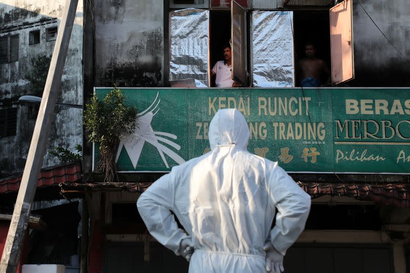 Residents look at a worker wearing a protective suit preparing for a disinfection operation, during the movement control order due to the outbreak of the coronavirus disease (COVID-19), in Kuala Lumpur