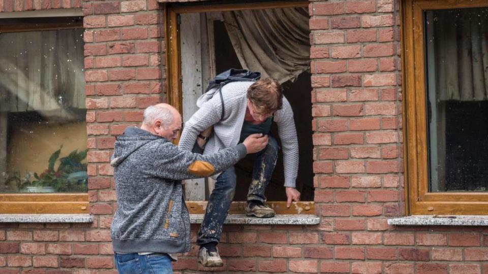 Un hombre ayuda a una mujer a trepar por una ventana tras las importantes inundaciones en Schuld