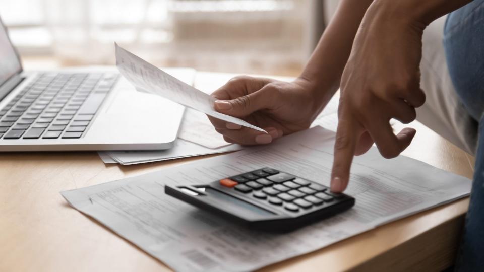 African woman holding in hand paper bills bank receipt using calculator on table calculate debt loan tax cost to pay manage finances concept doing accounting paperwork budget analysis, close up view.