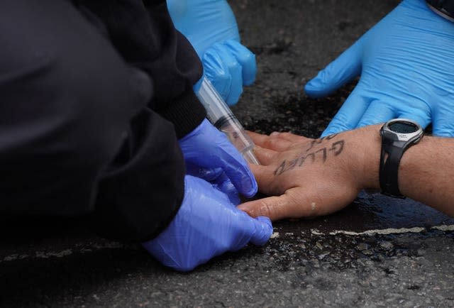 Police attempt to free a man who has glued himself to the road Ian West/PA)