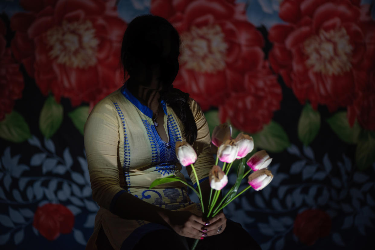S., her face in shadow, holds a bunch of tulips against a bold floral cloth in the background.
