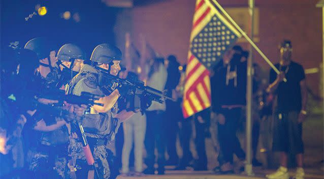 A police officer raises his weapon at a car speeding in his general direction as a more vocal and confrontational group of demonstrators stands on the sidewalk during further protests in reaction to the shooting of Michael Brown. Photo: Reuters.