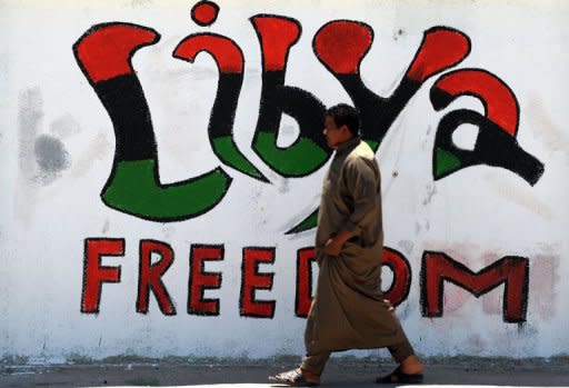 A Libyan man walks past graffiti in the eastern city of Ajdabiya. Moamer Kadhafi's regime reacted angrily Friday to a decision by world powers to provide funding to Libya's rebels, asserting that plans to tap assets frozen abroad were "piracy."