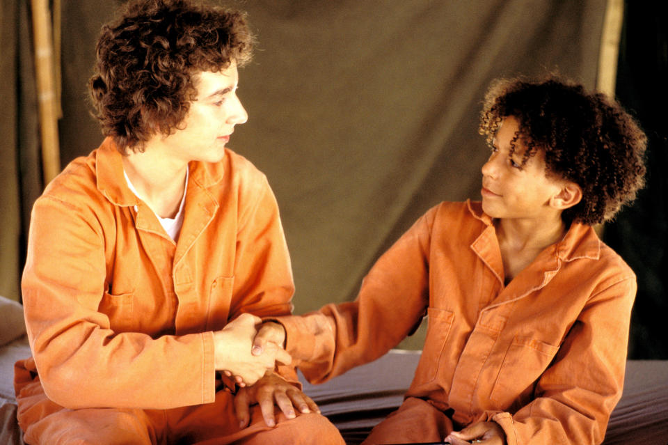 Shia as Stanley and Khleo Thomas as Hector Zeroni shaking hands while wearing matching orange jumpsuits