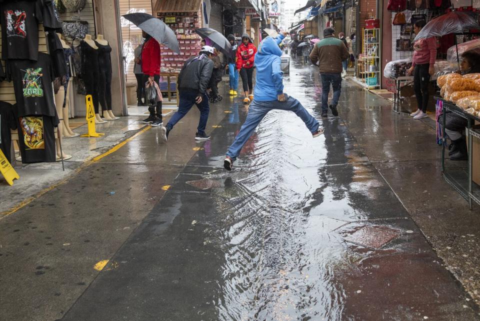 Brayan Suarez leaps to avoid getting wet while crossing to the other side as the rain water builds up on the ground